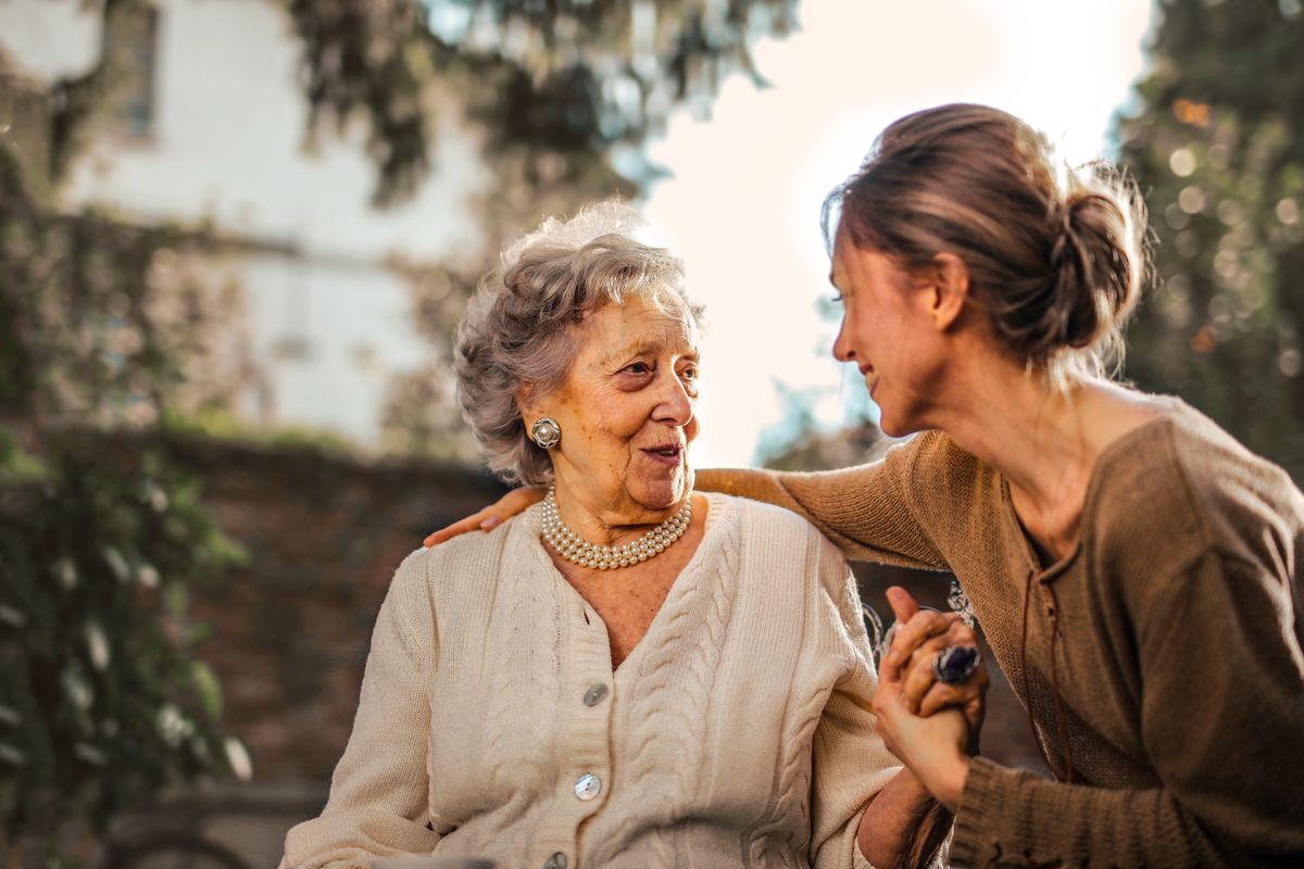 A younger woman caring for an elderly woman, holding her hand in a home garden