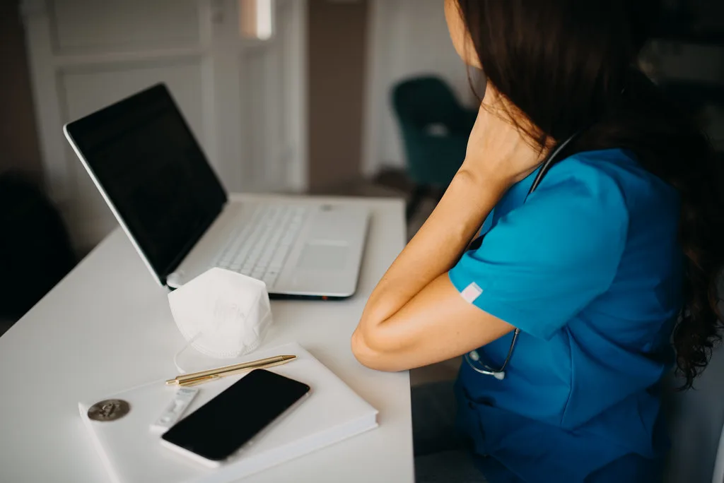 A nurse coordinating transitional care from hospital to home using a laptop and phone