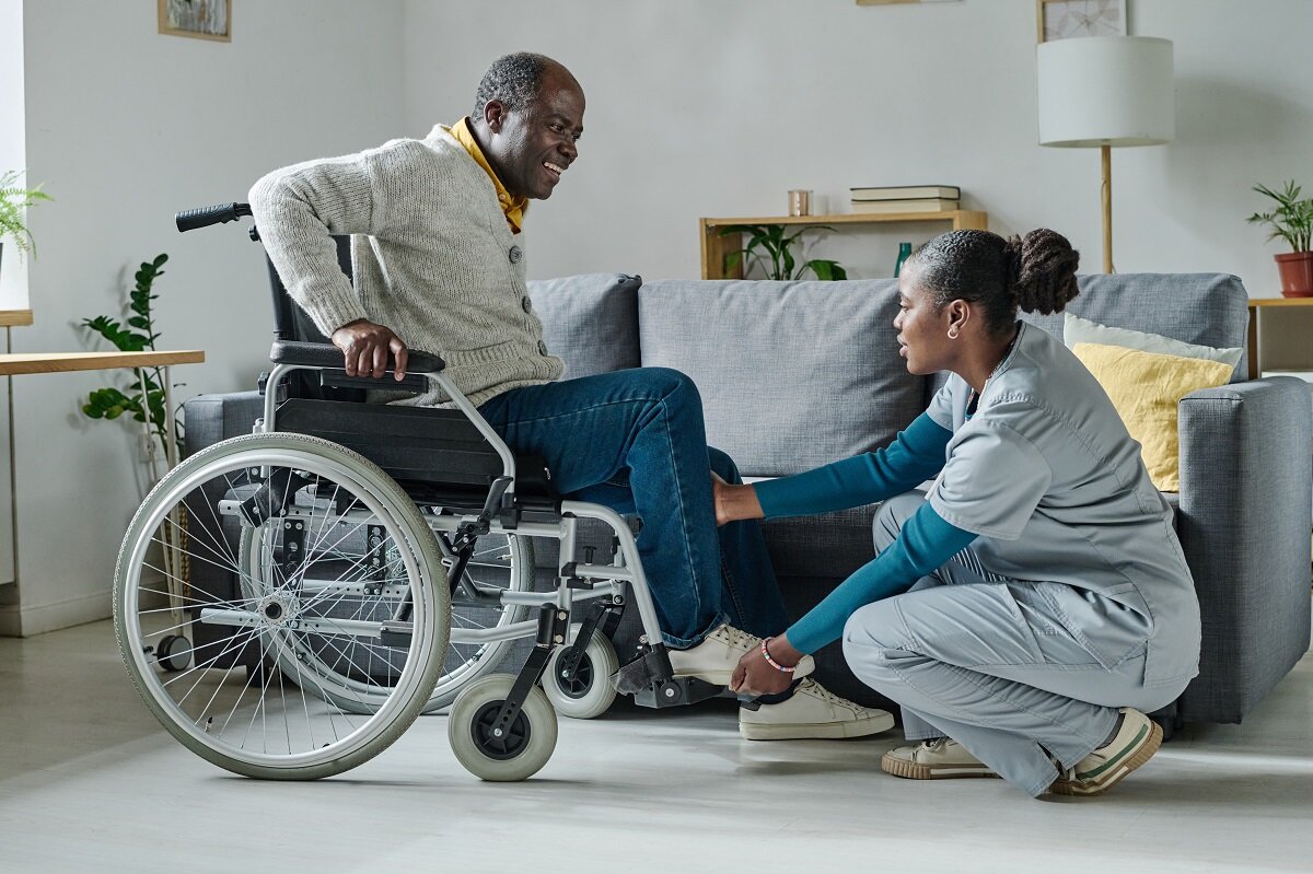 A caregiver in scrubs helping a senior with daily living tasks in a bright living room