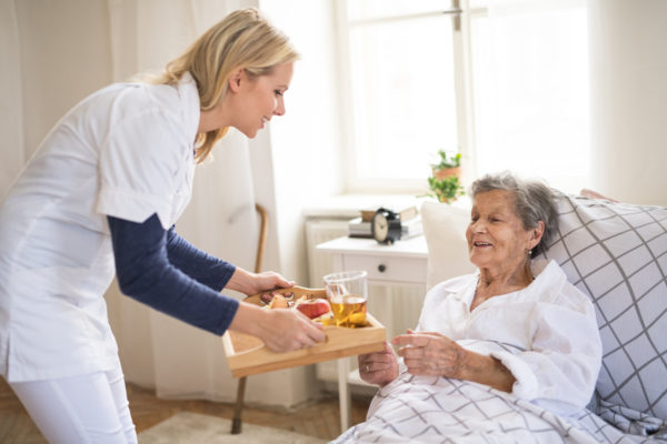 A caregiver serving a meal to a senior recovering in bed at home