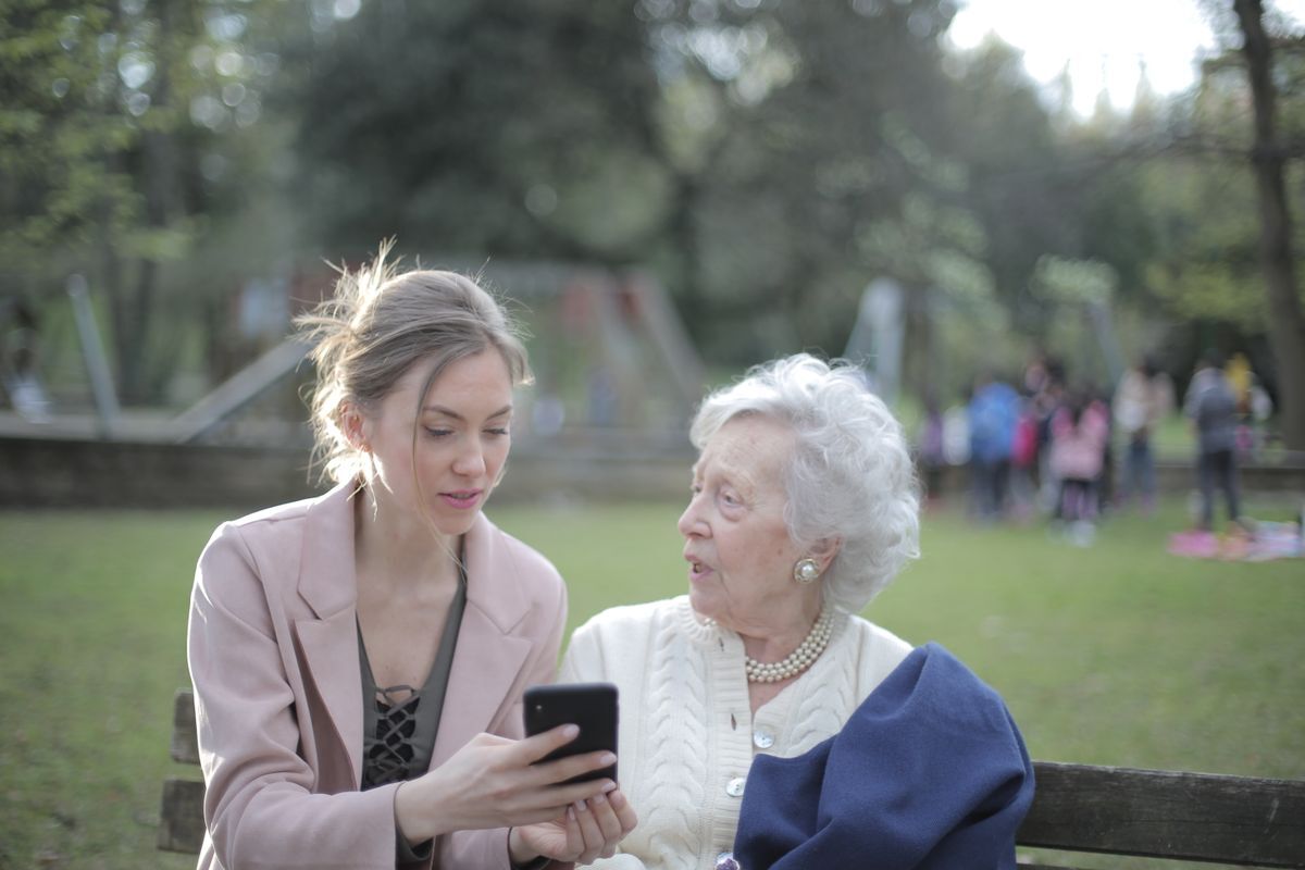 A caregiver sharing something on a phone with a senior woman, offering companionship and connection